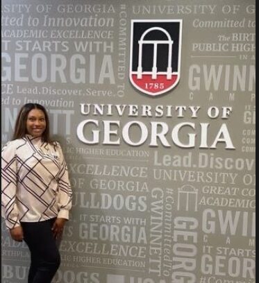 Woman standing in front of University of Georgia sign with logo and text background.