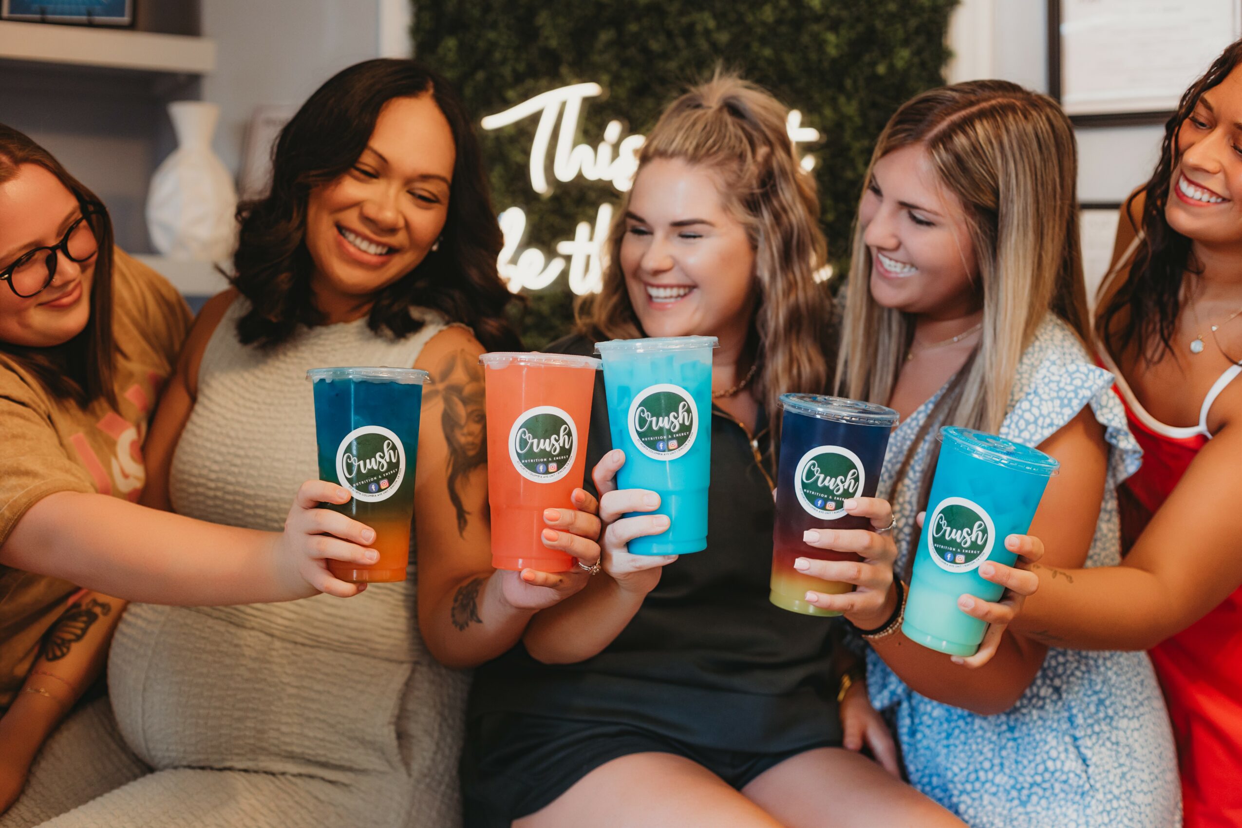 Group of women smiling and holding colorful drinks in a social setting.