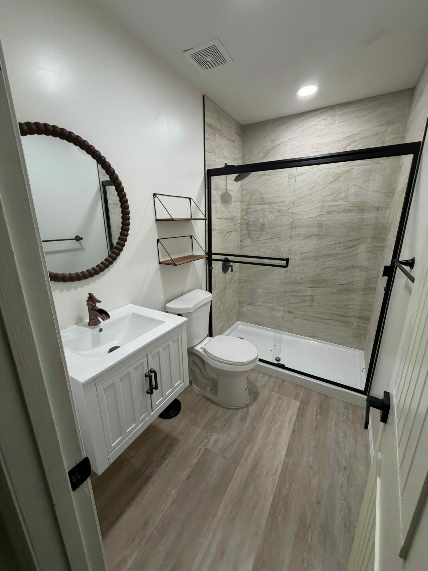 Bathroom with shower, toilet, sink, mirror, and wooden floor, viewed from doorway.