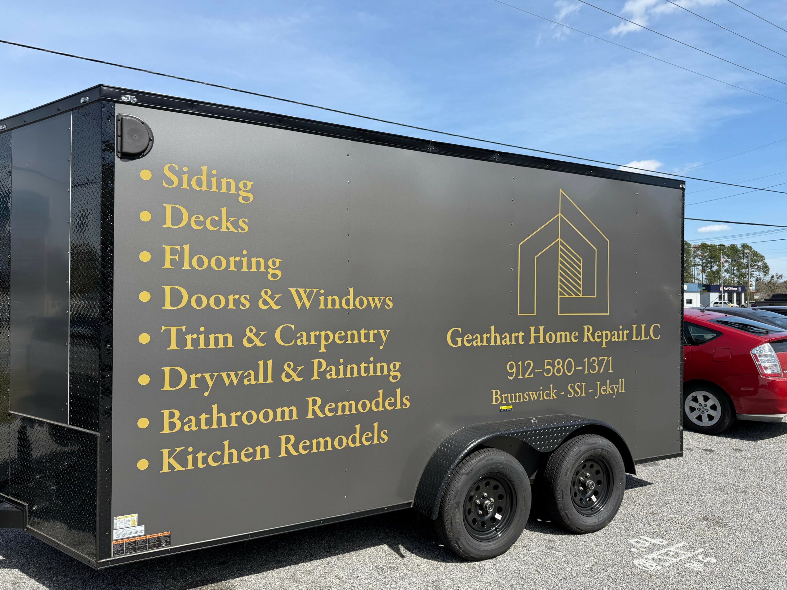 Black trailer with yellow text listing home renovation services and company contact information, parked outdoors.