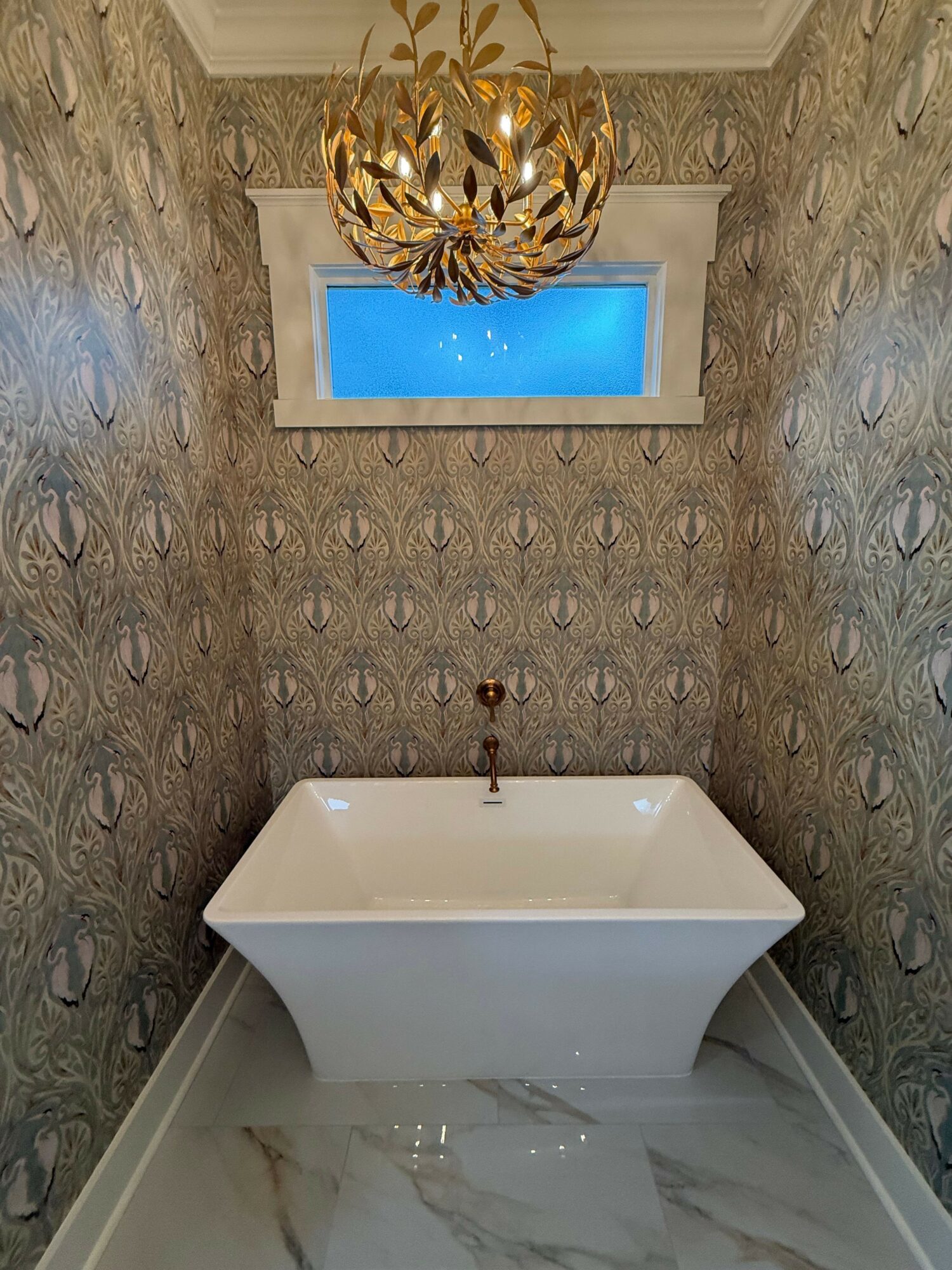 Bathroom with ornate wallpaper, a white bathtub, a small window, and a decorative chandelier ceiling light.