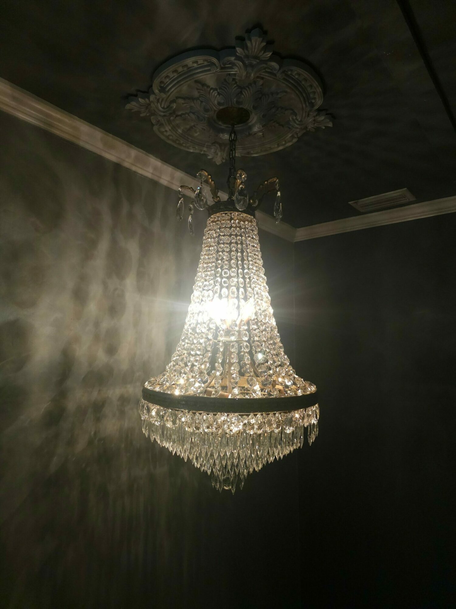 Elegant chandelier with multiple crystals hanging from a decorative fixture, illuminated and reflecting light onto the ceiling.