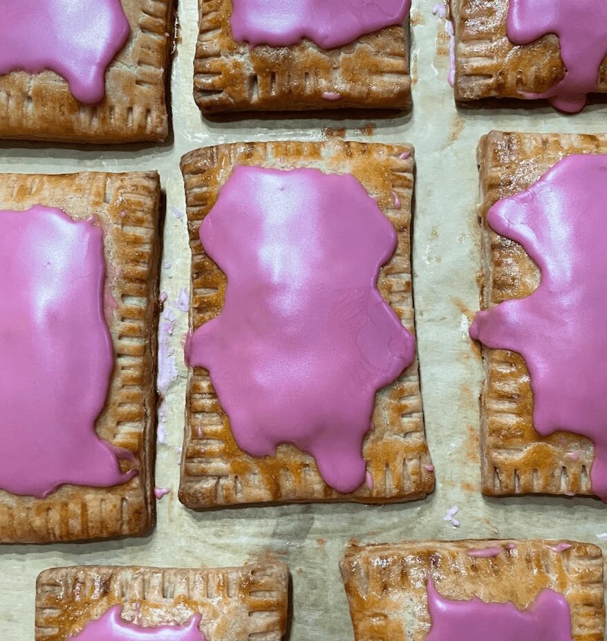 Rectangular cookies with pink icing, some with irregular shapes, on a baking sheet.