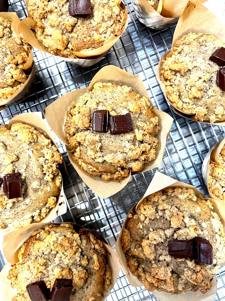 Several freshly baked cookies with chocolate chunks on a wire cooling rack, lined with parchment paper.