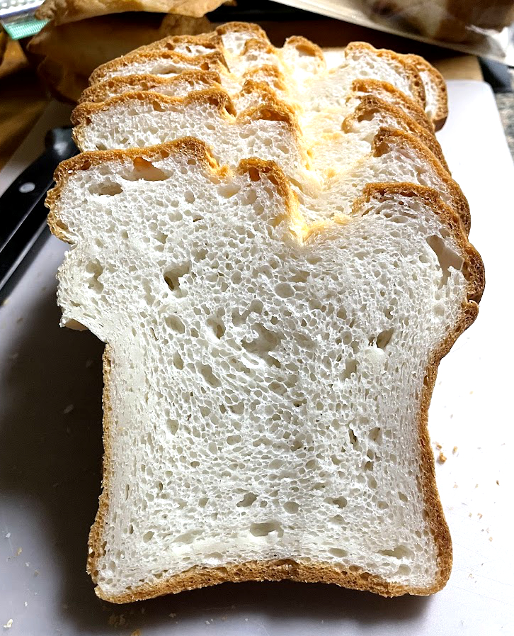 Sliced loaf of bread with a golden crust and airy interior, placed on a surface.