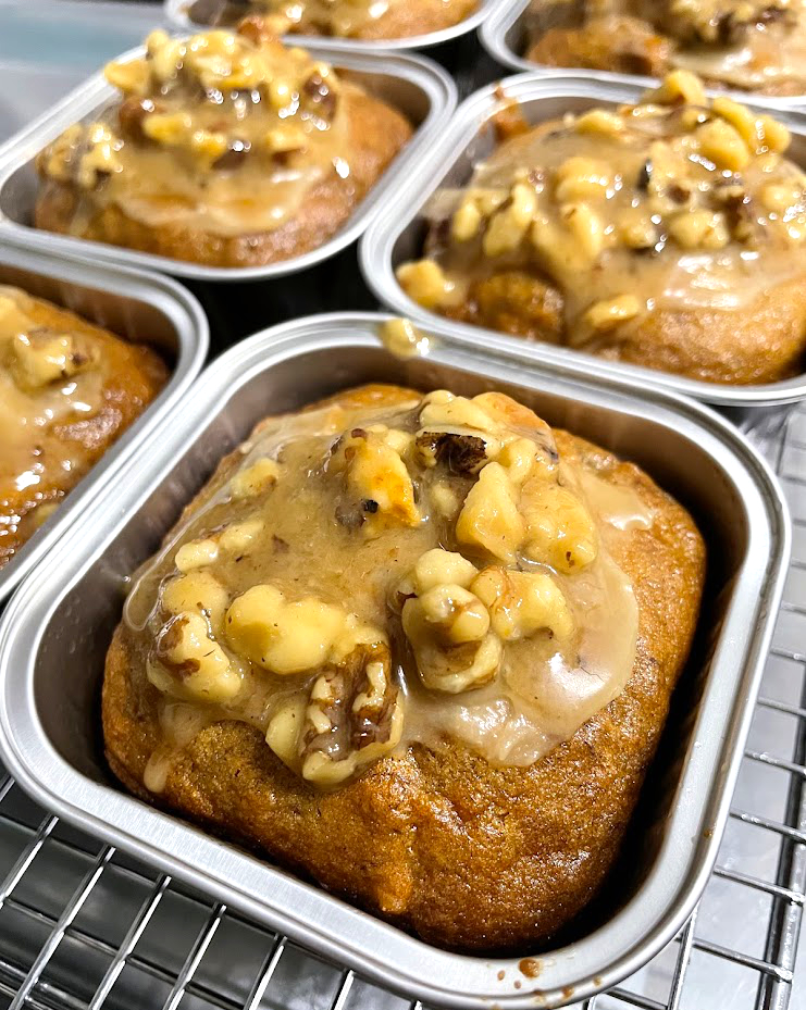Baked dessert with caramelized topping and chopped nuts in metal containers on a wire rack.