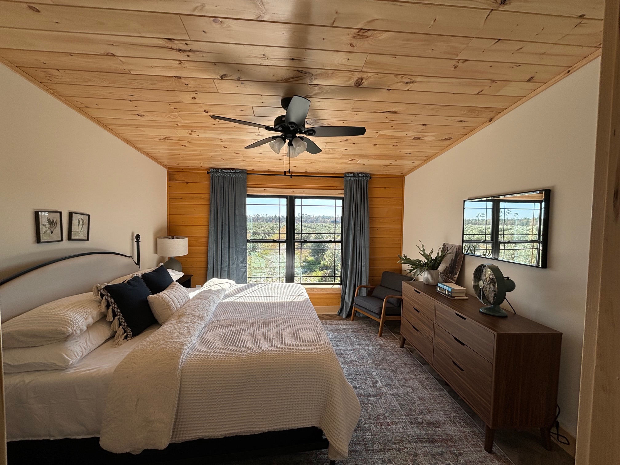 Bedroom with bed, dresser, mirror, window with curtains, ceiling fan, and wall decorations.