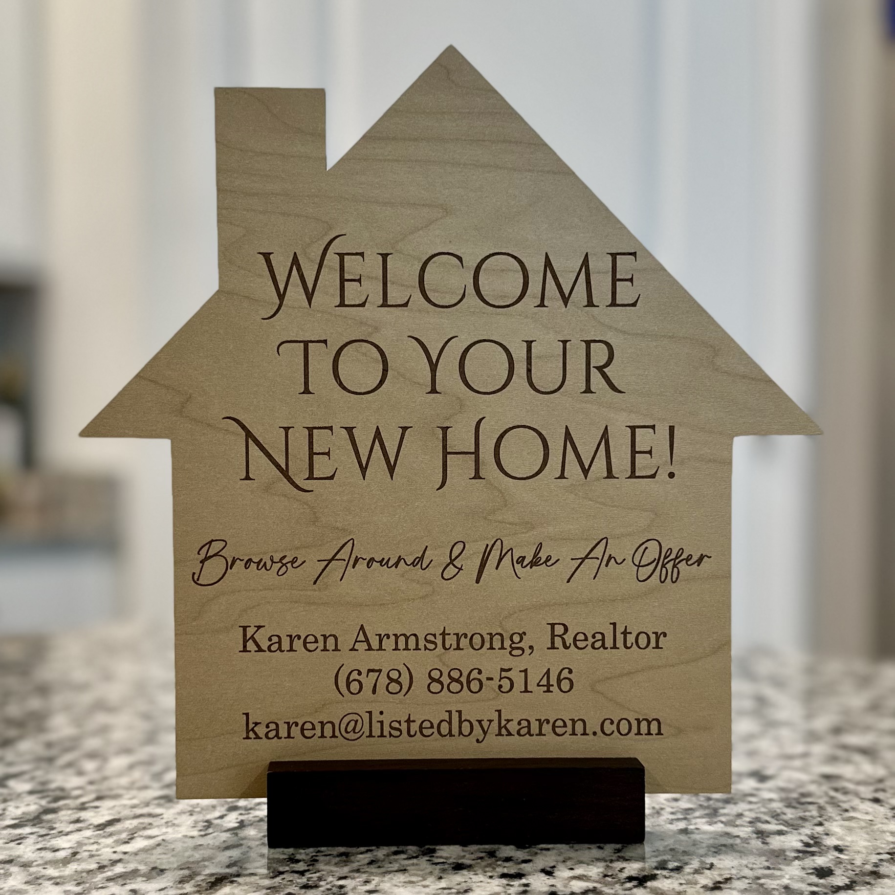 Wooden house-shaped sign with welcoming message and contact details on a countertop.