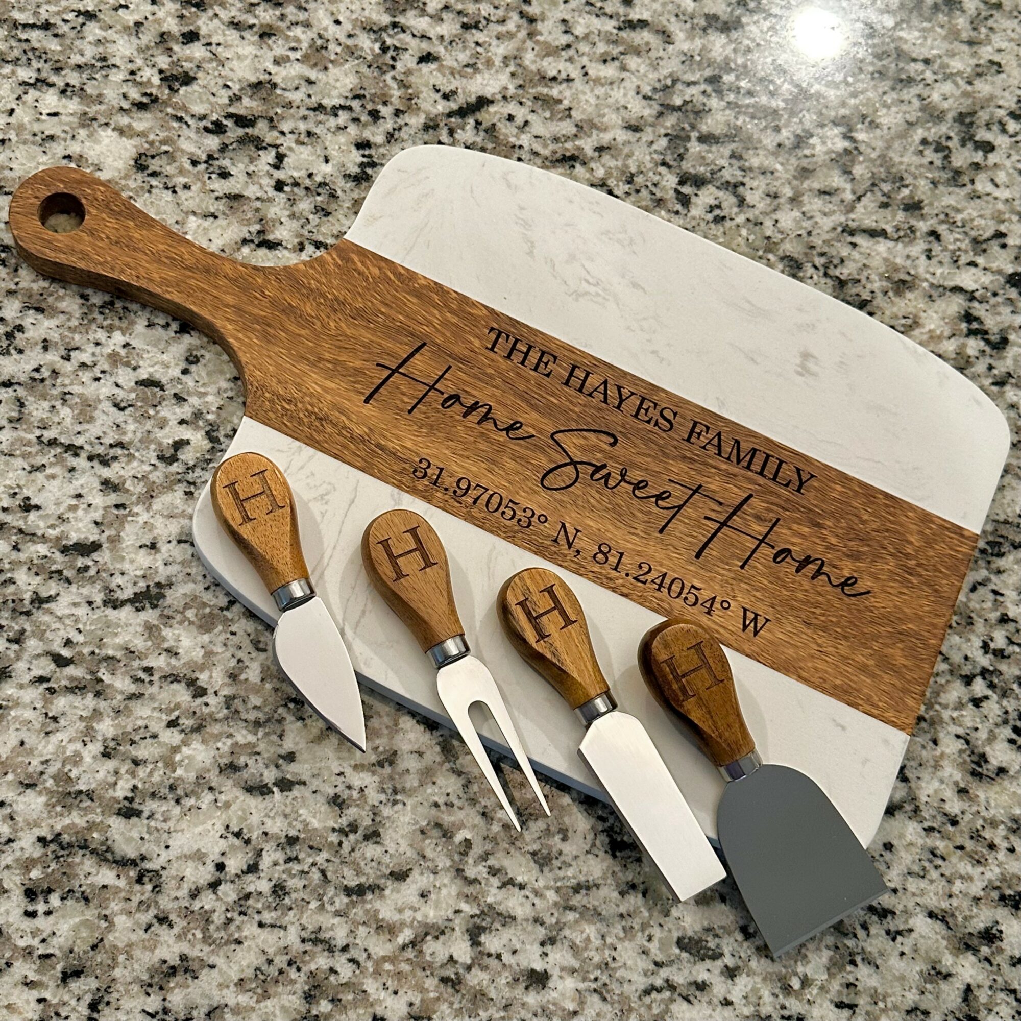Wooden cheese knives and a cutting board on a granite countertop, engraved with family name and contact details.