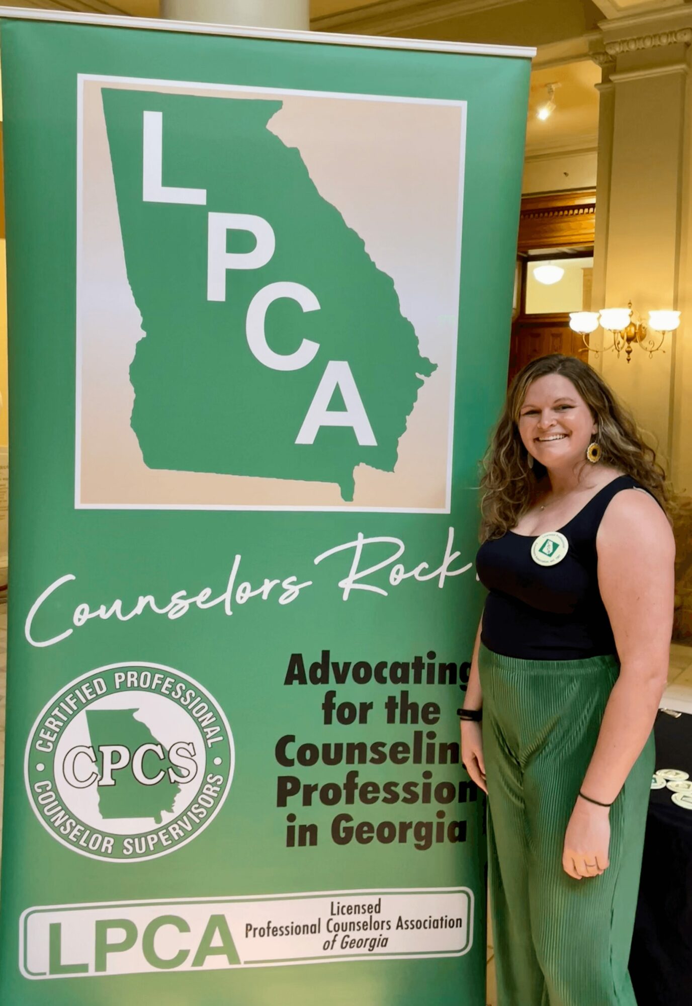 Woman standing next to a green and white banner with a map of Georgia, LPC, and CPCS logos, and text about counseling professionals.