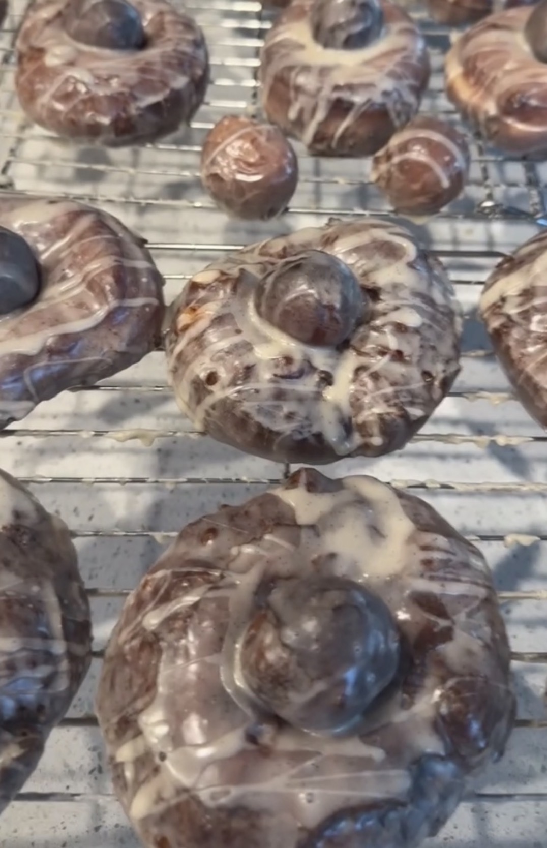 Chocolate-glazed donuts with a blueberry on top cooling on a wire rack.