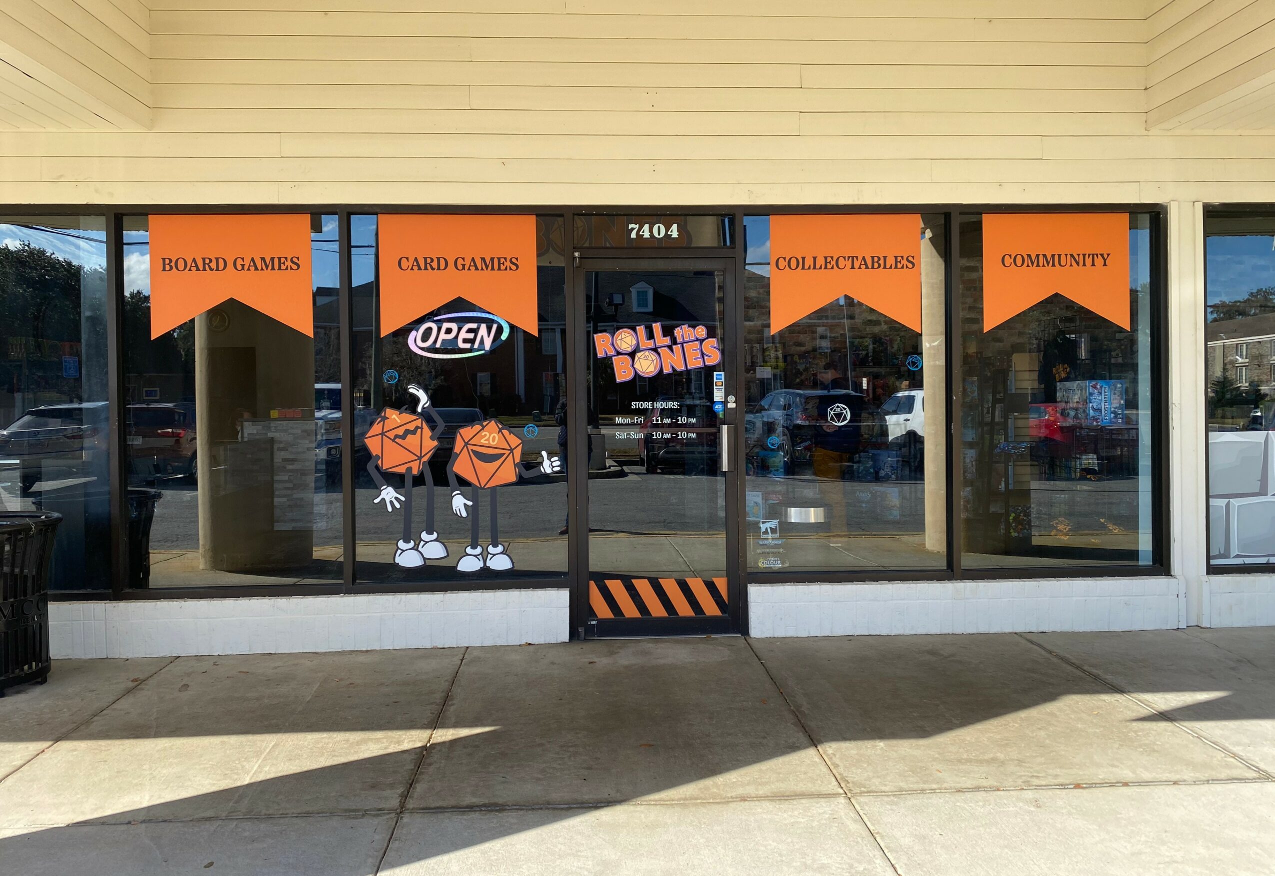 Store front with glass doors and windows, orange banners for board games, card games, collectibles, and community, and an open sign.