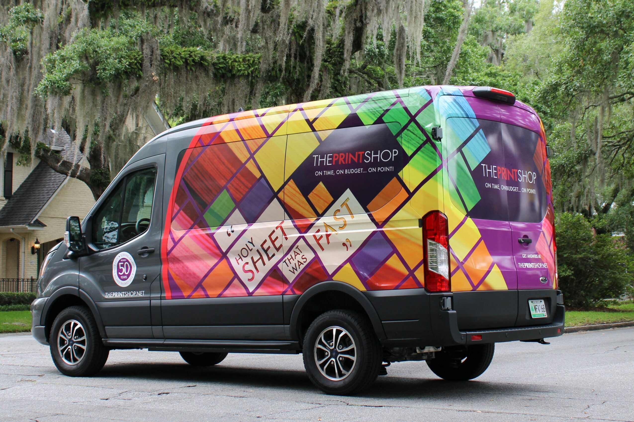 Colorful van with geometric patterns and text, parked outdoors with trees in the background.