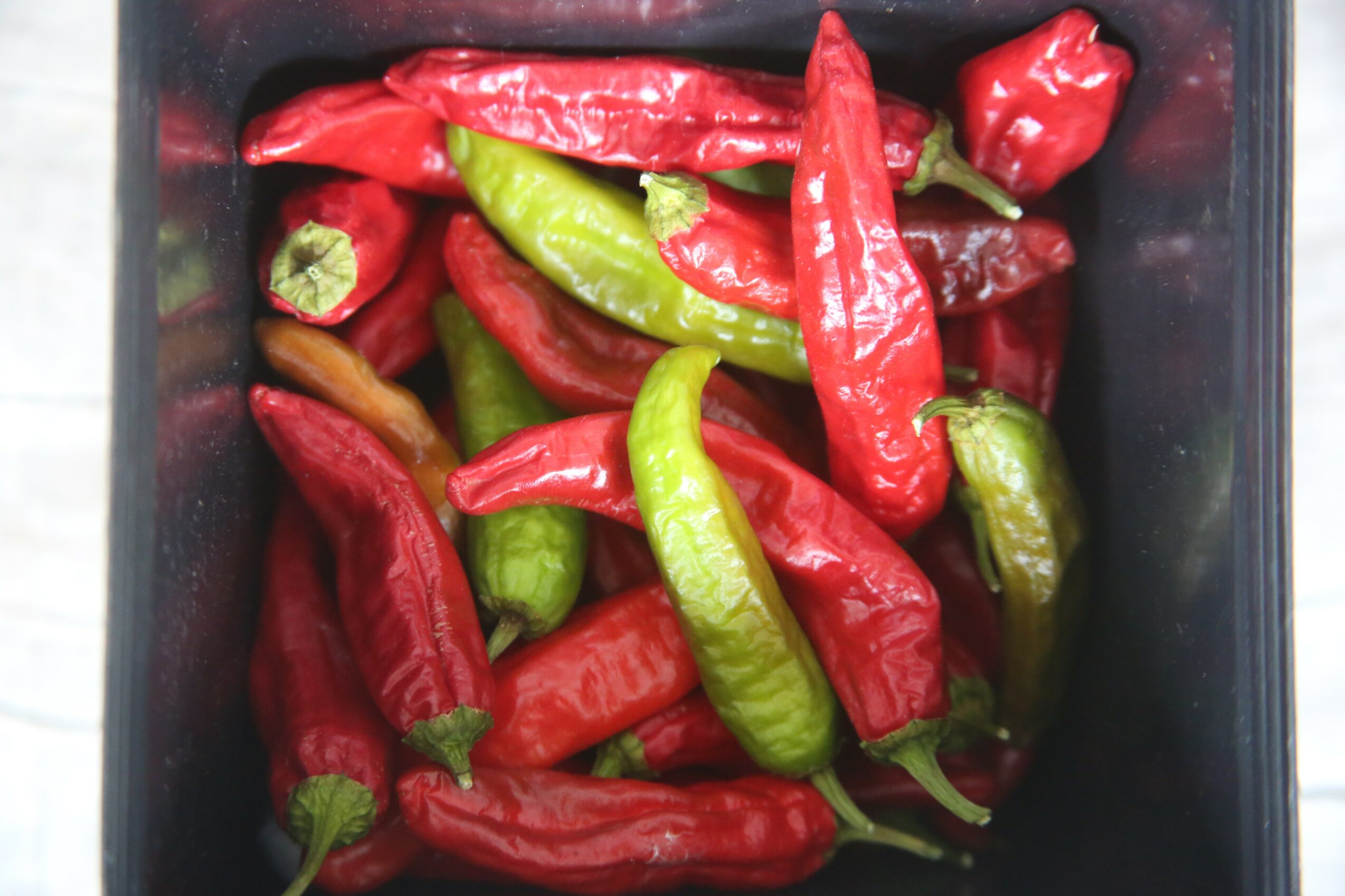 A container filled with red and green chili peppers, some with stems attached.