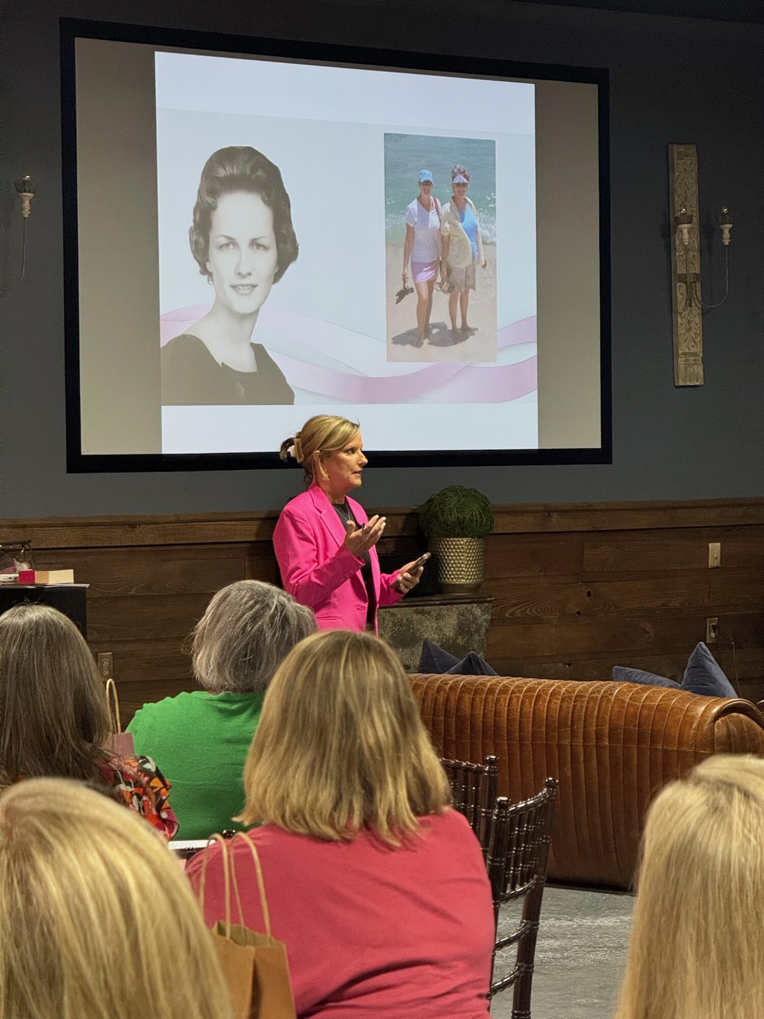 Woman in pink jacket presenting in front of audience with a slide showing a portrait and a beach photo.