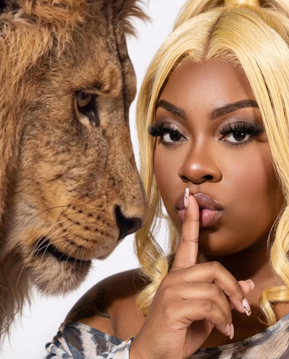 Woman with blonde hair holding finger to lips, lion close-up facing her, both looking at each other, white background.