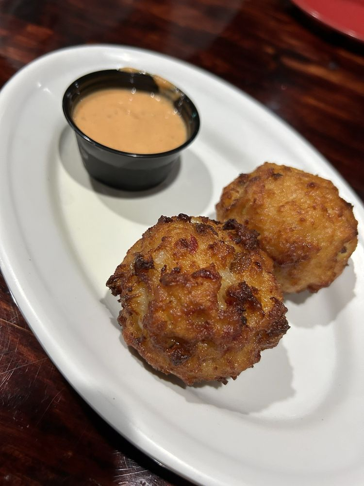 Two fried croquettes with dipping sauce on a white plate, dark wooden table background.