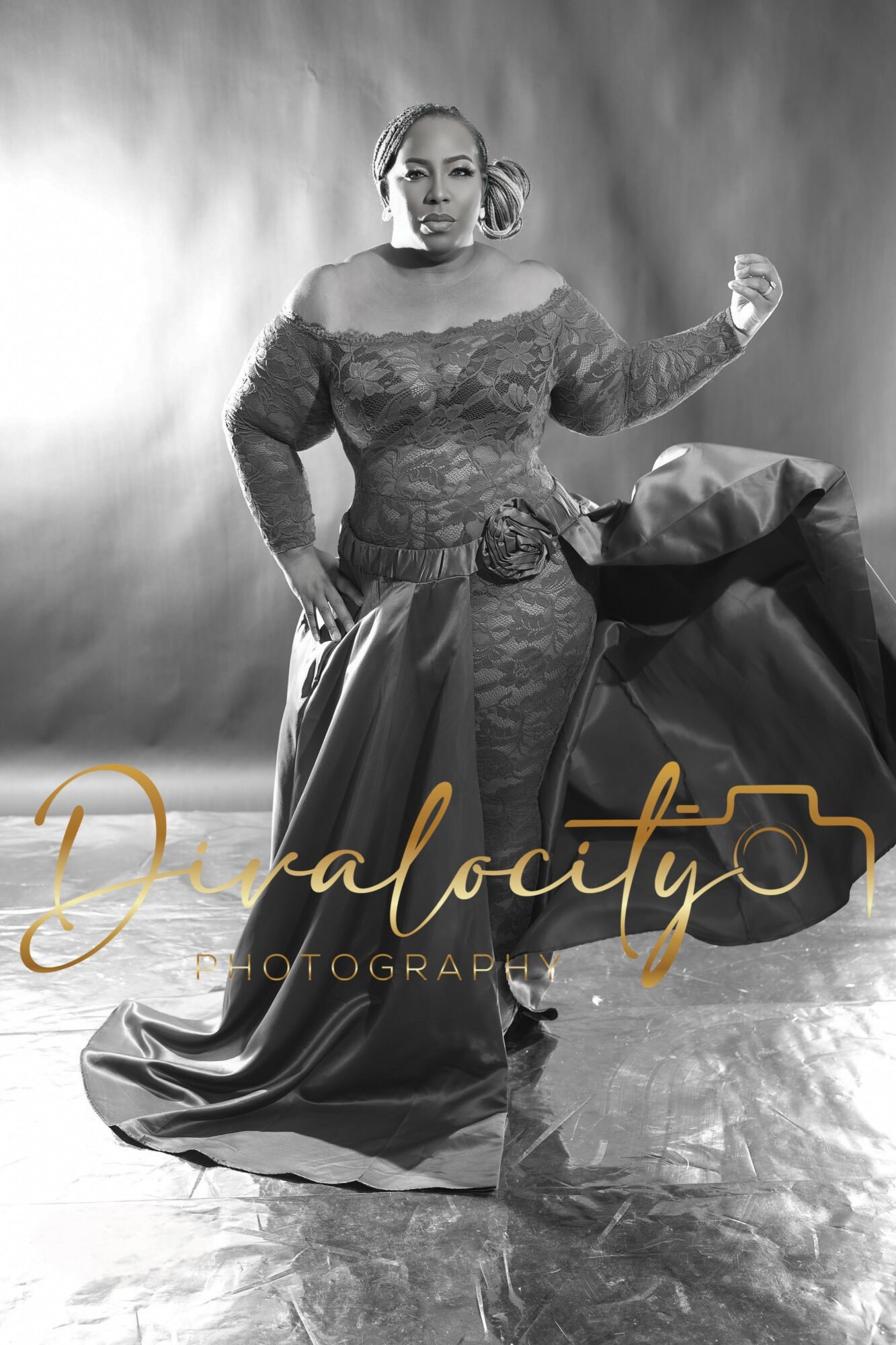 Woman in elegant dress standing with one arm raised, holding a large fabric piece, in a studio with a smoky background.