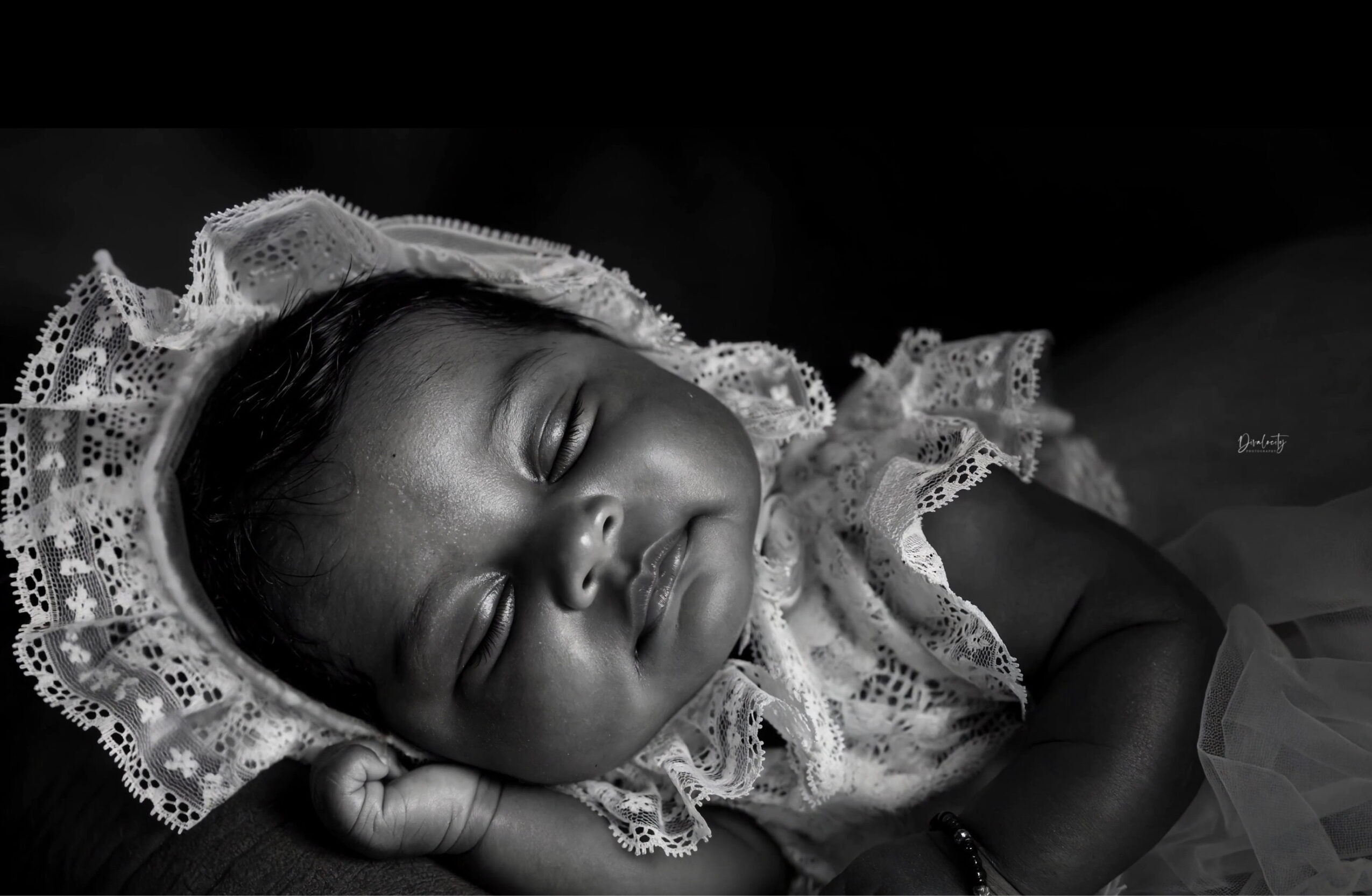 Baby girl with lace bonnet sleeping peacefully, lying on her side, in black and white, with a soft expression.
