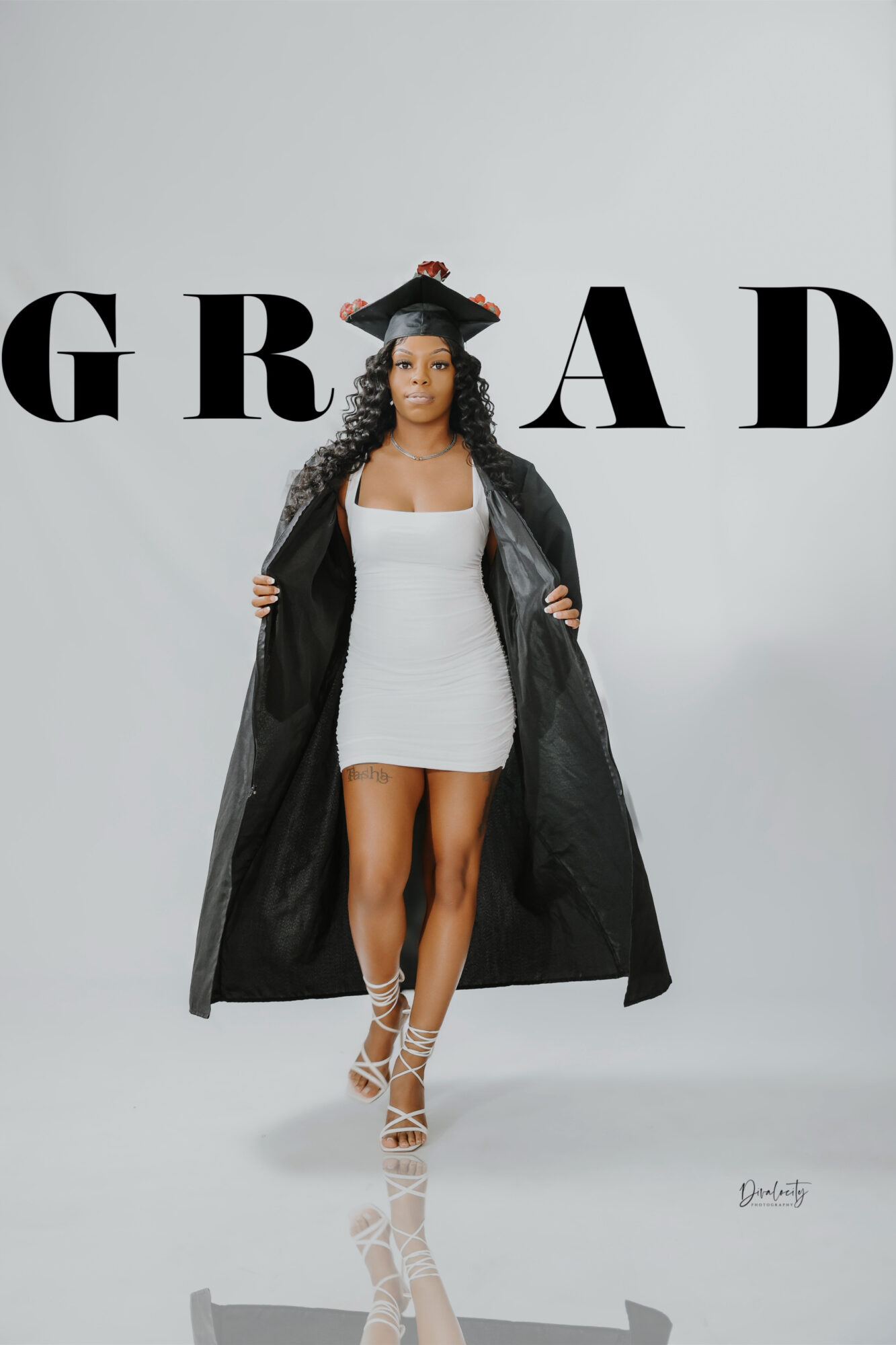Woman in a white dress and black coat standing in front of a gray background with large black letters.