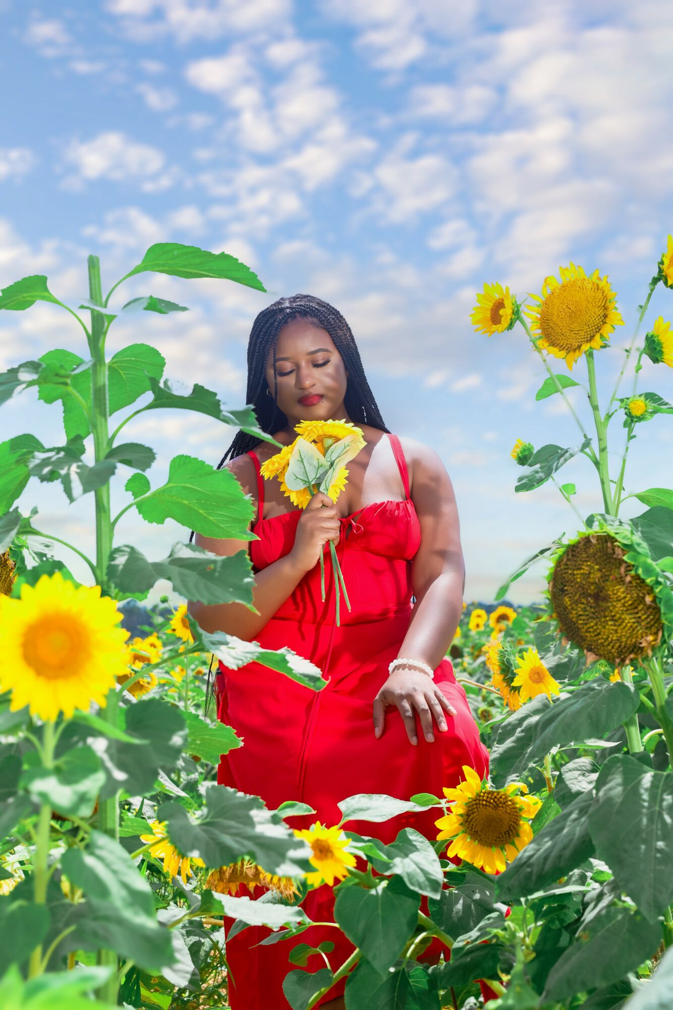 Woman in red dress holding sunflower in a sunflower field under a blue sky with clouds